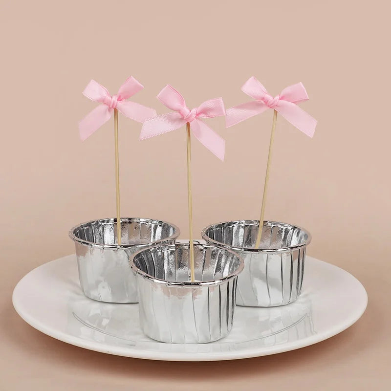 Three pink bow cupcake toppers displayed on a white plate.