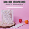 A collection of white paper lollipop sticks for cake pops is displayed in a clear container on a pink background.