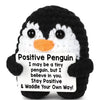 A black and white crocheted penguin toy with a sign that reads Positive Penguin I may be a tiny penguin but I believe in you 
