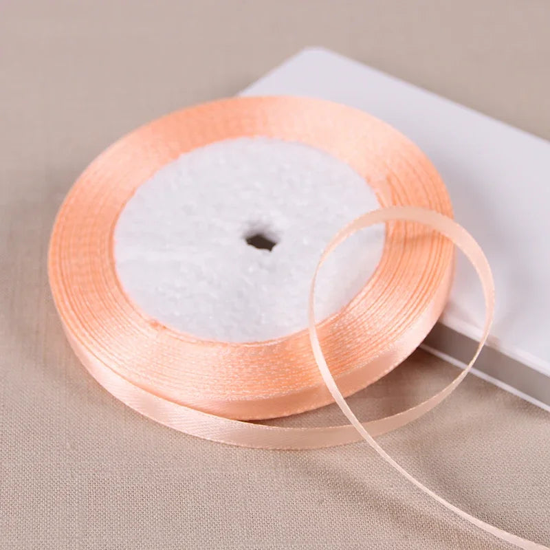 A spool of satin ribbon for gift wrapping and DIY crafts, showing the orange ribbon rolled on a white core.