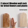 A wooden wall rack for dried flowers and plants with an arched design mounted on a white wall.