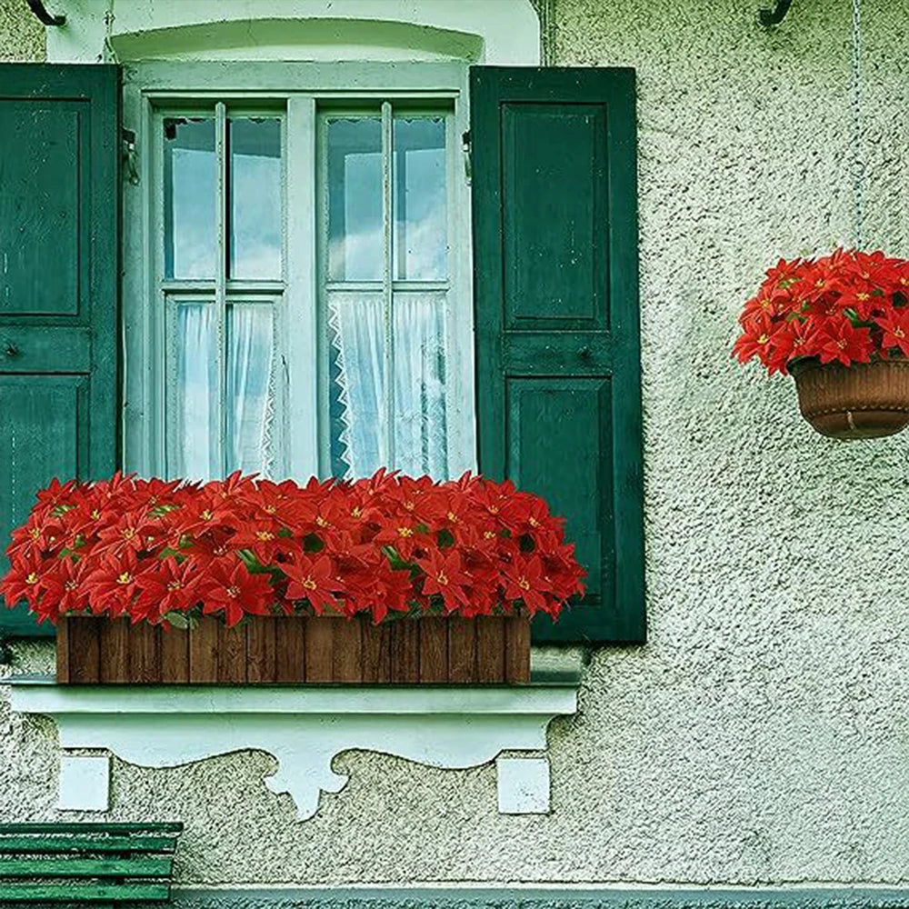 A window frame decorated with green shutters and a planter overflowing with bright red artificial poinsettia flowers.