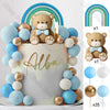 A white cake decorated with blue and gold ball accents and a bear topper, set with rainbow arch decorations.