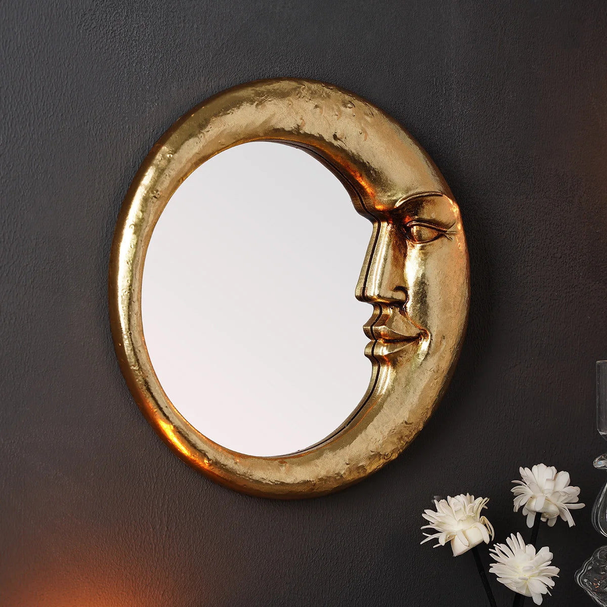 A round, golden decorative wall mirror with a crescent moon shape mounted on a dark gray wall.