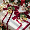 Festive Christmas curtain tie-backs with red bows, pinecones, and gold ornaments arranged on a white tablecloth.
