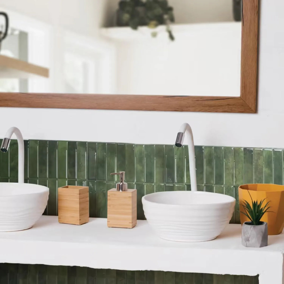 A white bathroom vanity with a green tile backsplash, featuring modern faucets and wooden soap dispensers.
