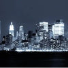 A nighttime view of the New York City skyline with illuminated skyscrapers across a dark body of water.