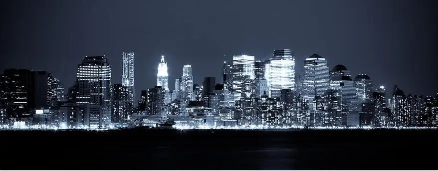 A nighttime view of the New York City skyline with illuminated skyscrapers across a dark body of water.