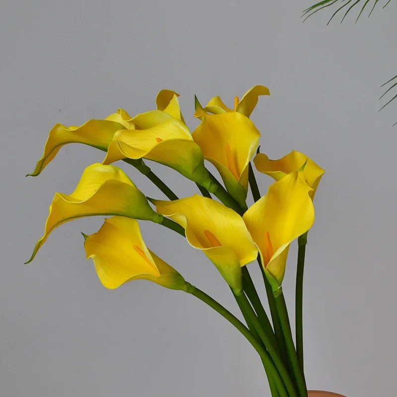 A bunch of yellow artificial calla lily stems with green leaves against a gray background.