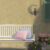 A black cat silhouette with a crescent moon is displayed as wall decor on a beige stucco wall above a white bench.