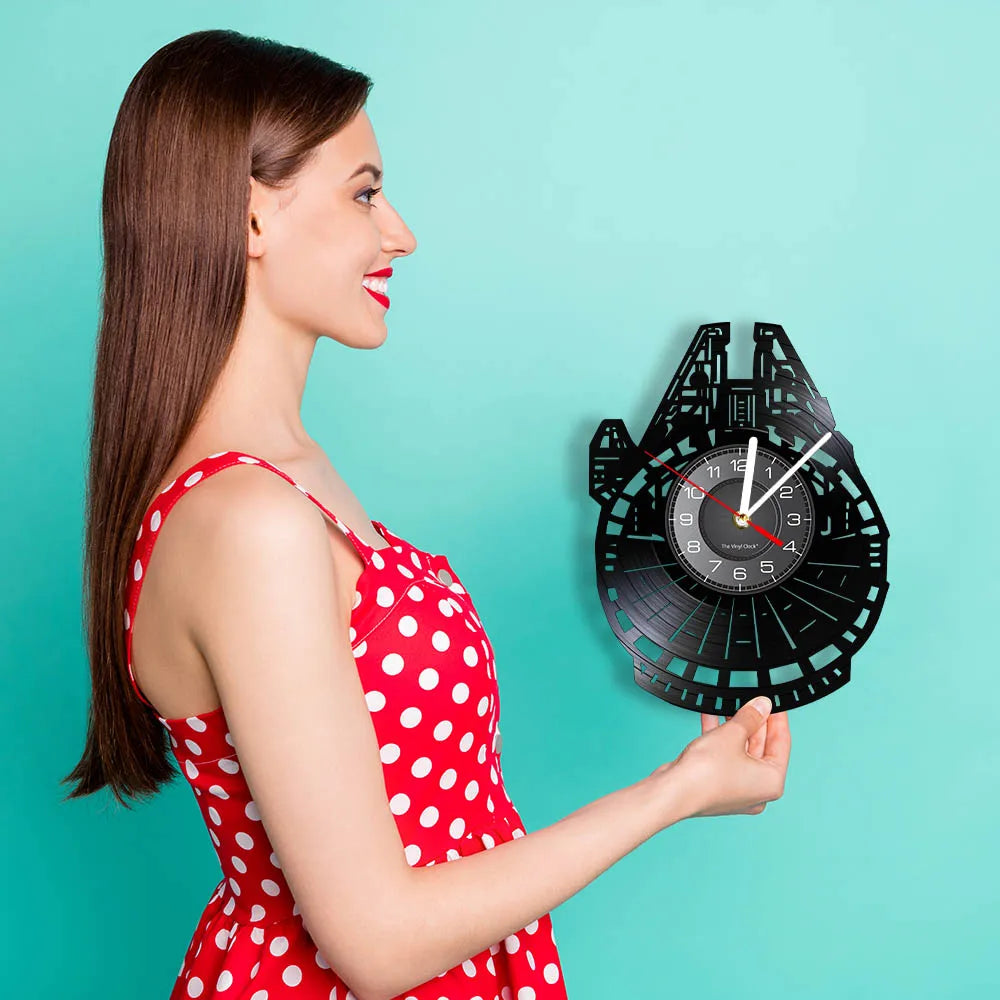 A woman holds a black vinyl record wall clock against a teal background.