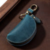 A dark teal Crazy Horse leather key pouch with a brass carabiner attached, resting on a brown surface.