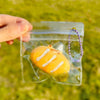 A hand holds a clear plastic pouch containing an orange cartoon food squeeze toy keychain.