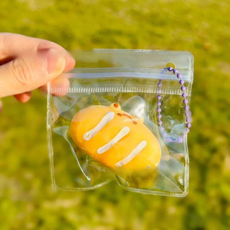 A hand holds a clear plastic pouch containing an orange cartoon food squeeze toy keychain.