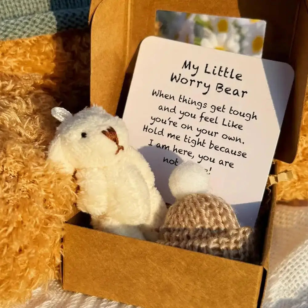Un pequeño oso de peluche blanco está sentado en una caja de cartón junto a una tarjeta inspiradora.