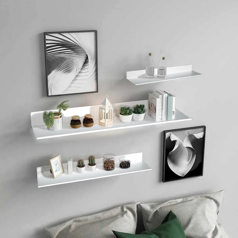 A gallery wall featuring three white floating shelves displaying various decorative items and framed artwork on a gray wall.
