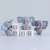 Three gray elephant figurines with blue ears stand next to three white blocks labeled B BABY Y.