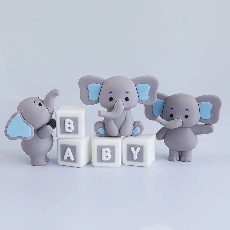 Three gray elephant figurines with blue ears stand next to three white blocks labeled B BABY Y.