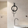 Schwarze minimalistische geometrische Wandskulptur mit konzentrischen Kreisen und vertikalen Linien an einer weißen Fliesenwa