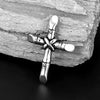 A silver stainless steel cross necklace pendant resting on a weathered piece of wood.