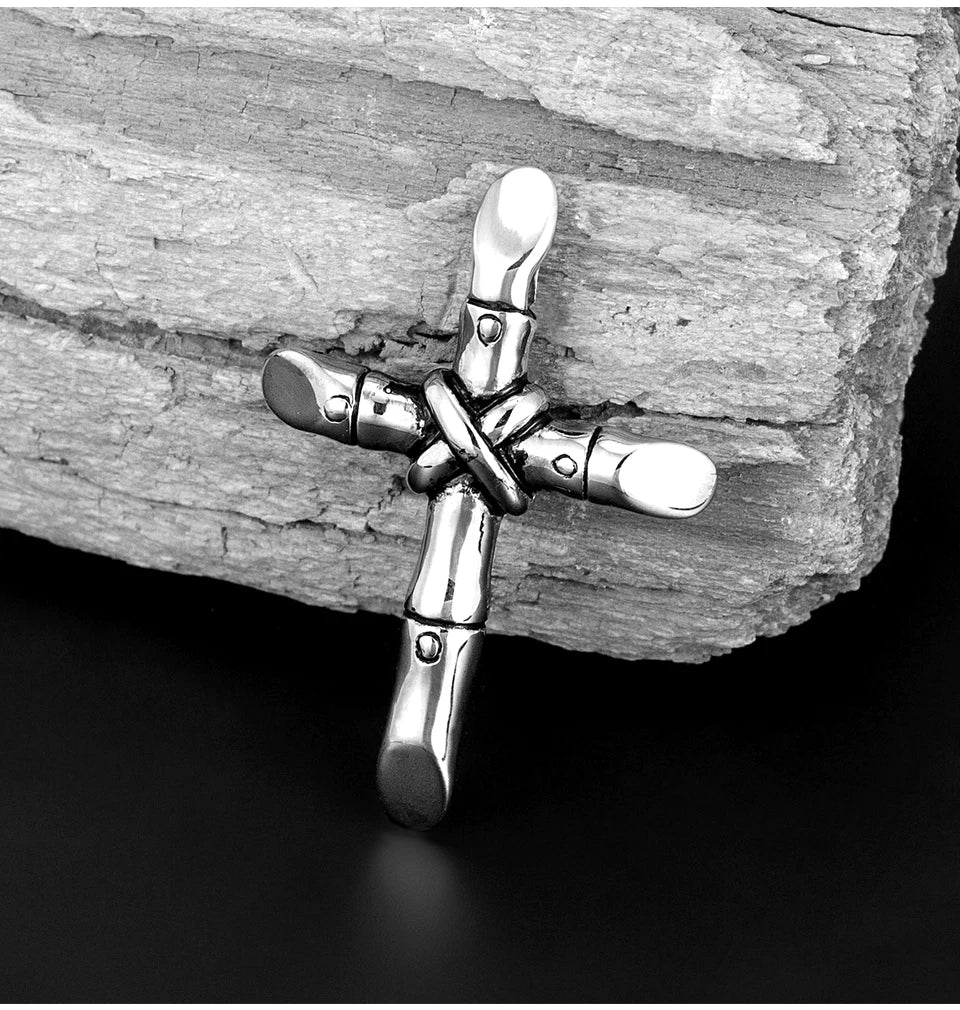 A silver stainless steel cross necklace pendant resting on a weathered piece of wood.