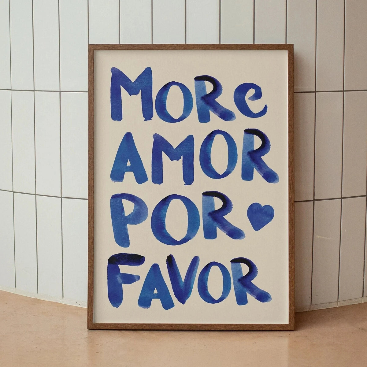A framed canvas print featuring the text MORE AMOR POR FAVOR written in blue script on light beige paper.