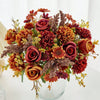 A vibrant bouquet of artificial silk flowers in shades of deep red, burnt orange, and dusty rose.
