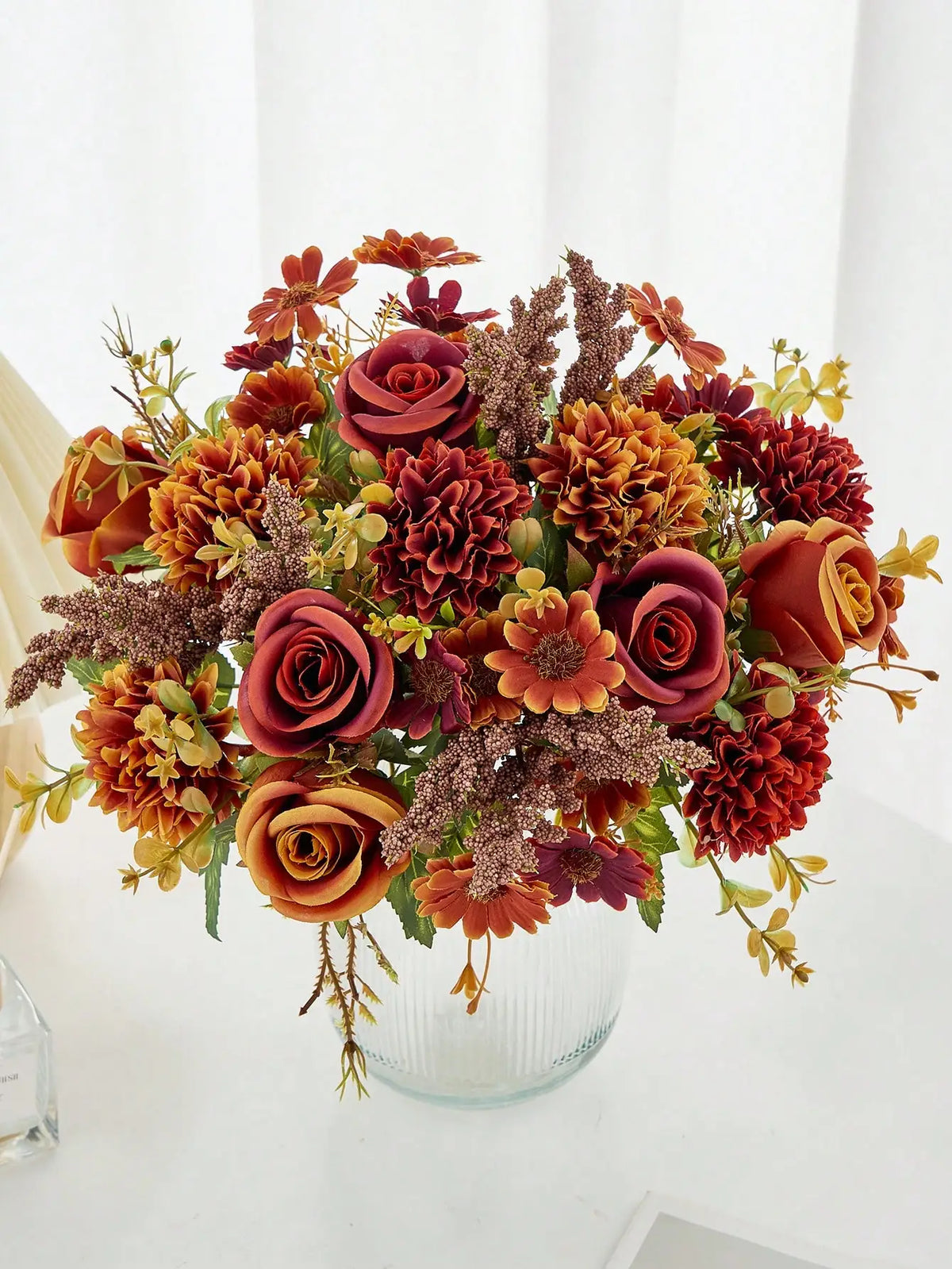 A vibrant bouquet of artificial silk flowers in shades of deep red, burnt orange, and dusty rose.