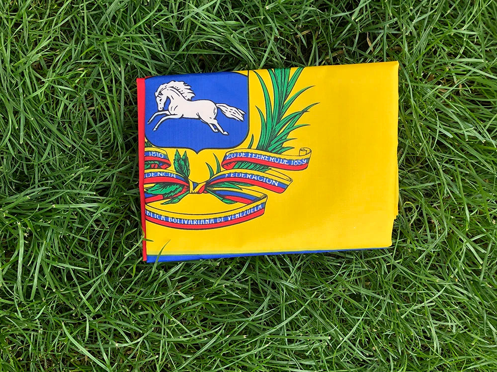 A yellow banner featuring the flag of Venezuela with green palm leaves and text on a green grassy background.