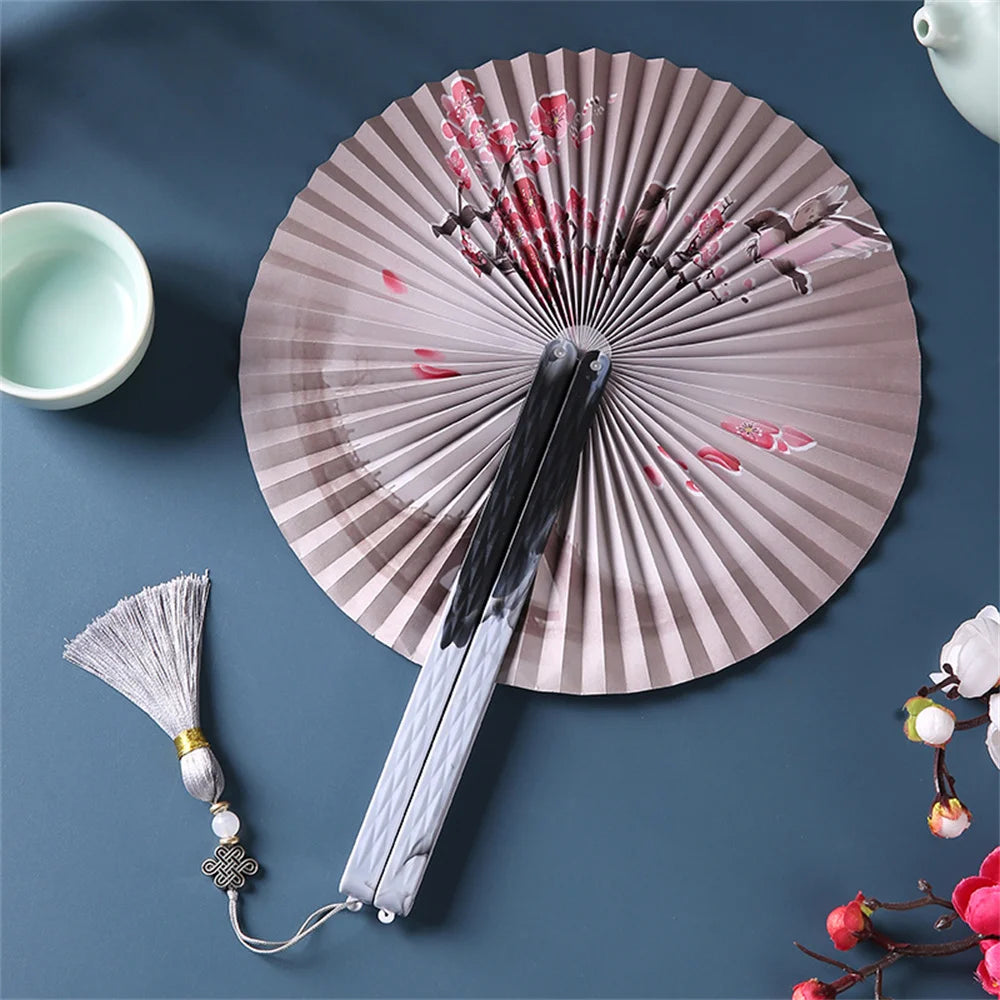 Traditional Chinese folding fan with a dark and pink design resting on a dark blue surface.