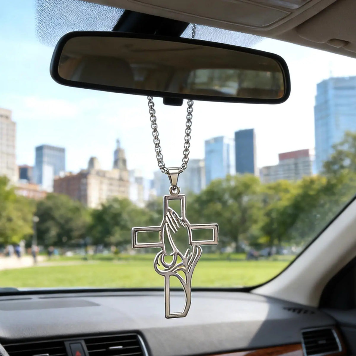 Stainless steel praying hands cross pendant hanging from a chain displayed in a car mirror.