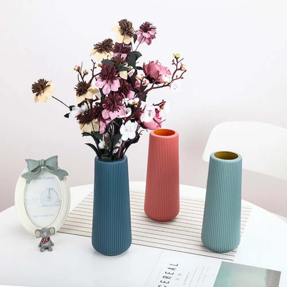 A modern, ribbed plastic flower vase in dark blue holds dried flowers on a white surface.
