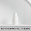 White ceramic tabletop vase with a smooth, tapered shape displayed on a white shelf.