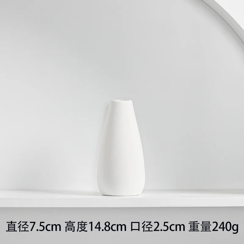 White ceramic tabletop vase with a smooth, tapered shape displayed on a white shelf.