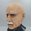 A realistic latex mask of an old man with white hair and a mustache, displayed on a black stand.