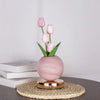 Pink tulips in a smooth pink vase on a woven mat and wooden surface.