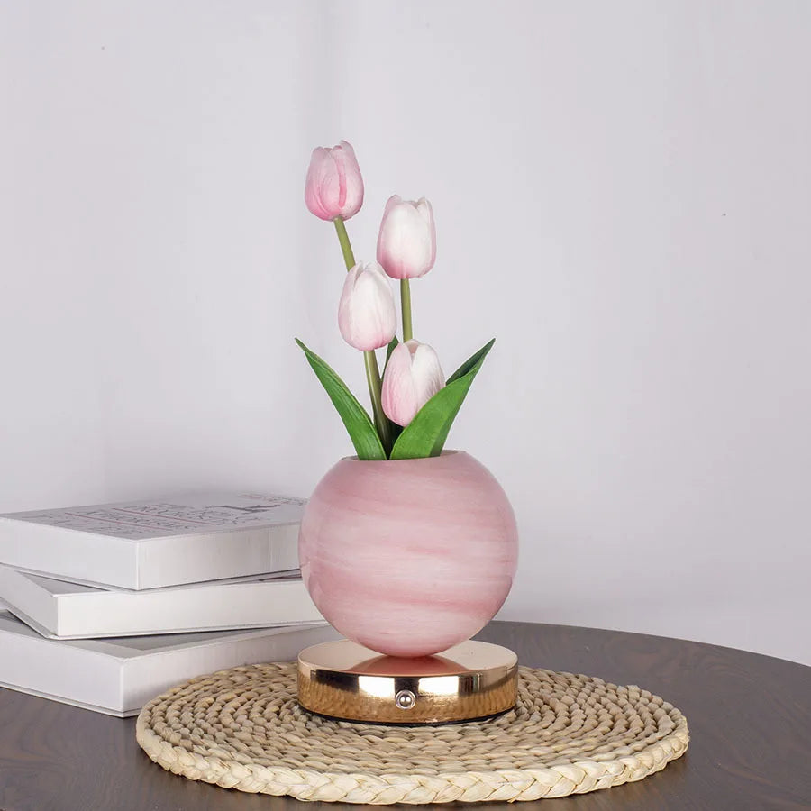 Pink tulips in a smooth pink vase on a woven mat and wooden surface.