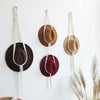 Three macrame hat organizers with wooden dowels are displayed as boho wall hangings against a white background.