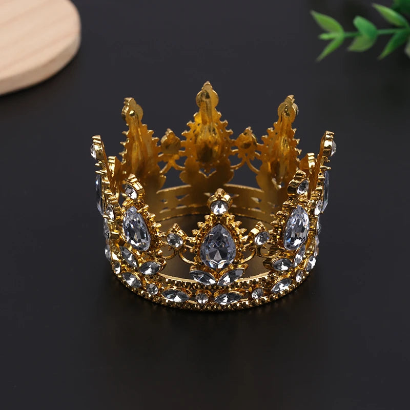 A golden crown tiara with clear stones is displayed on a dark surface.