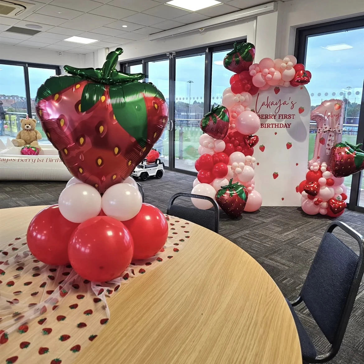 عرض قوس بالونات بمناسبة الفراولة، يضم بالونات حمراء وخضراء وبالون فراولة كبير.