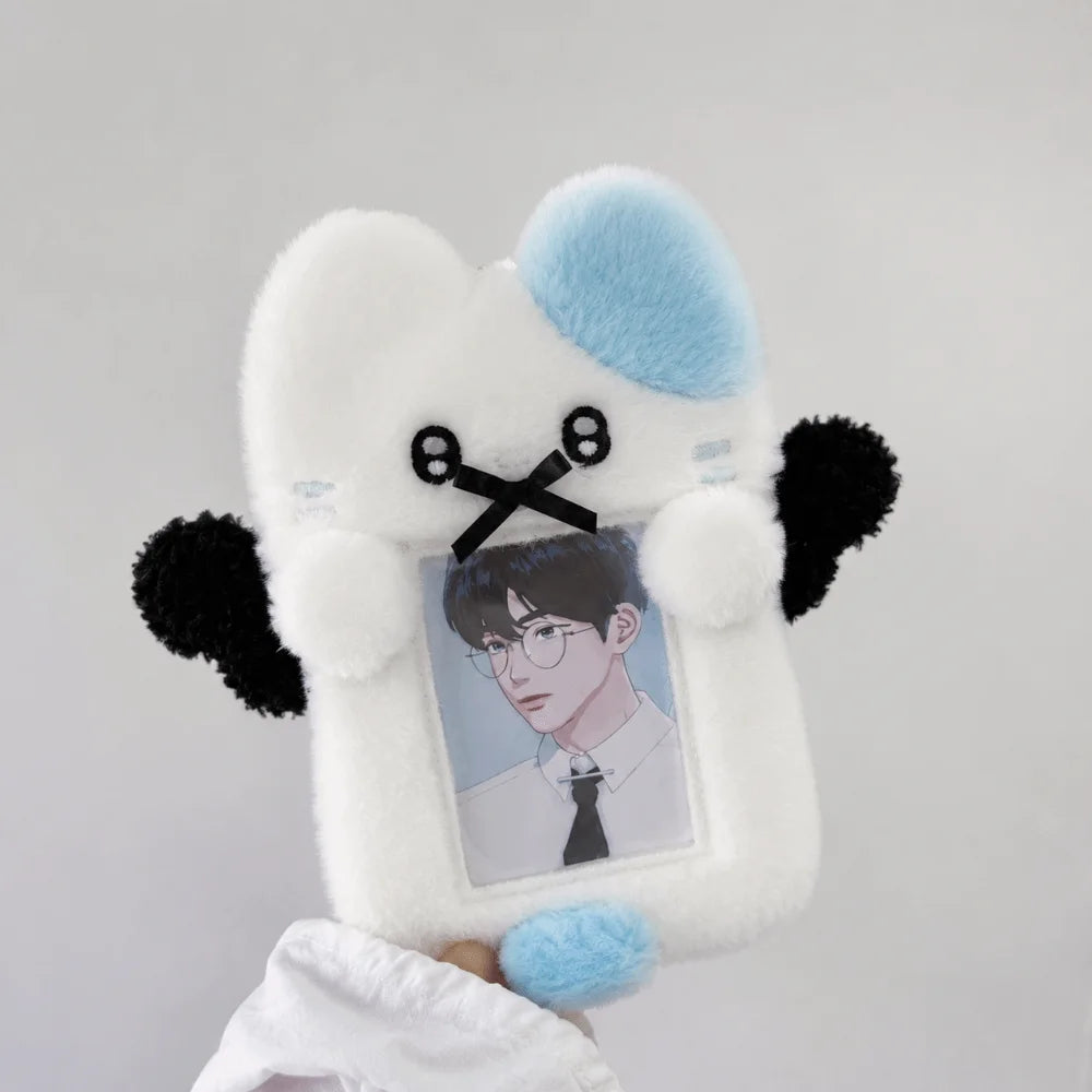 A white and light blue plush toy shaped like a cat holding a framed photo of a man.