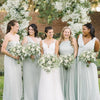 A group of women in light green dresses posing outdoors surrounded by white baby's breath flowers.