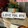 A distressed white wooden sign with the text LOVE YOU BYE rests on burlap fabric next to a potted plant.