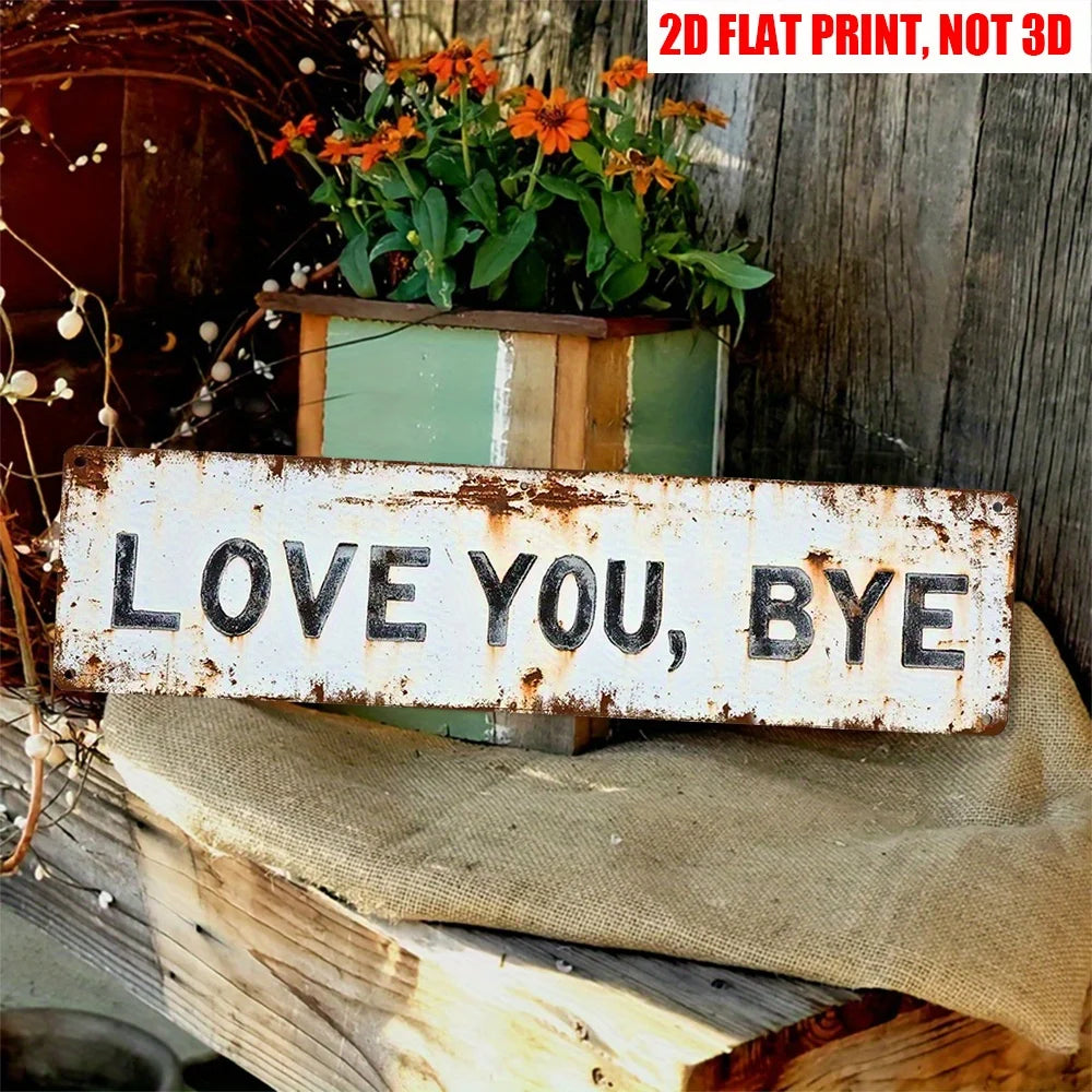A distressed white wooden sign with the text LOVE YOU BYE rests on burlap fabric next to a potted plant.