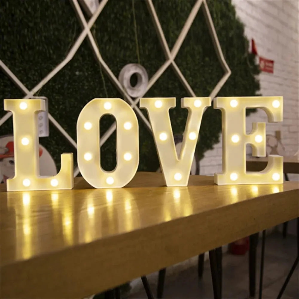 Large luminous LED alphabet letters spelling LOVE displayed on a wooden surface against a green backdrop
