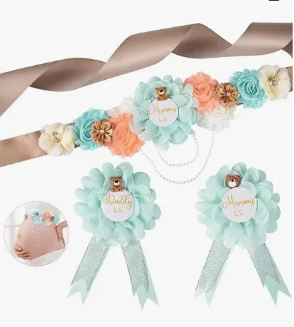 A set of floral maternity sash and corsage pins featuring blue, peach, and cream roses on a sheer ribbon.