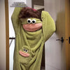 A person wearing a green fuzzy monster onesie pajama with large eyes and pink features.