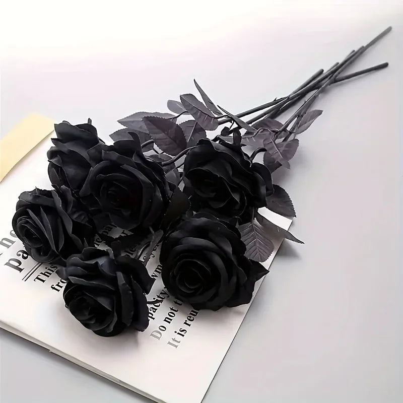 A bunch of artificial black roses with dark green leaves displayed on a white background.
