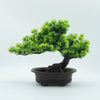 A small, vibrant green artificial bonsai tree planted in a black pot.