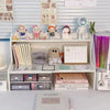 A white two-layer desktop organizer shelf displaying various stationery, small figures, and desk accessories.